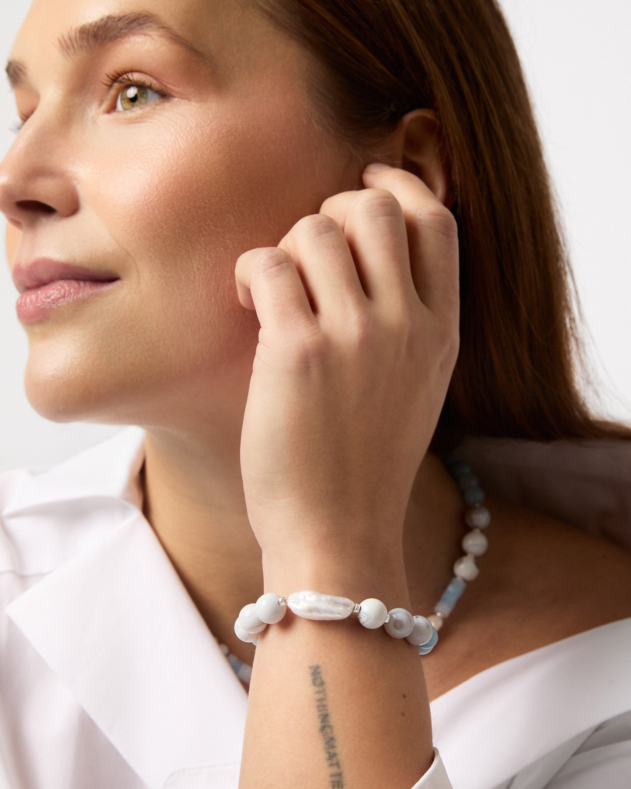 Woman wearing a white and blue beaded bracelet on a plain background
