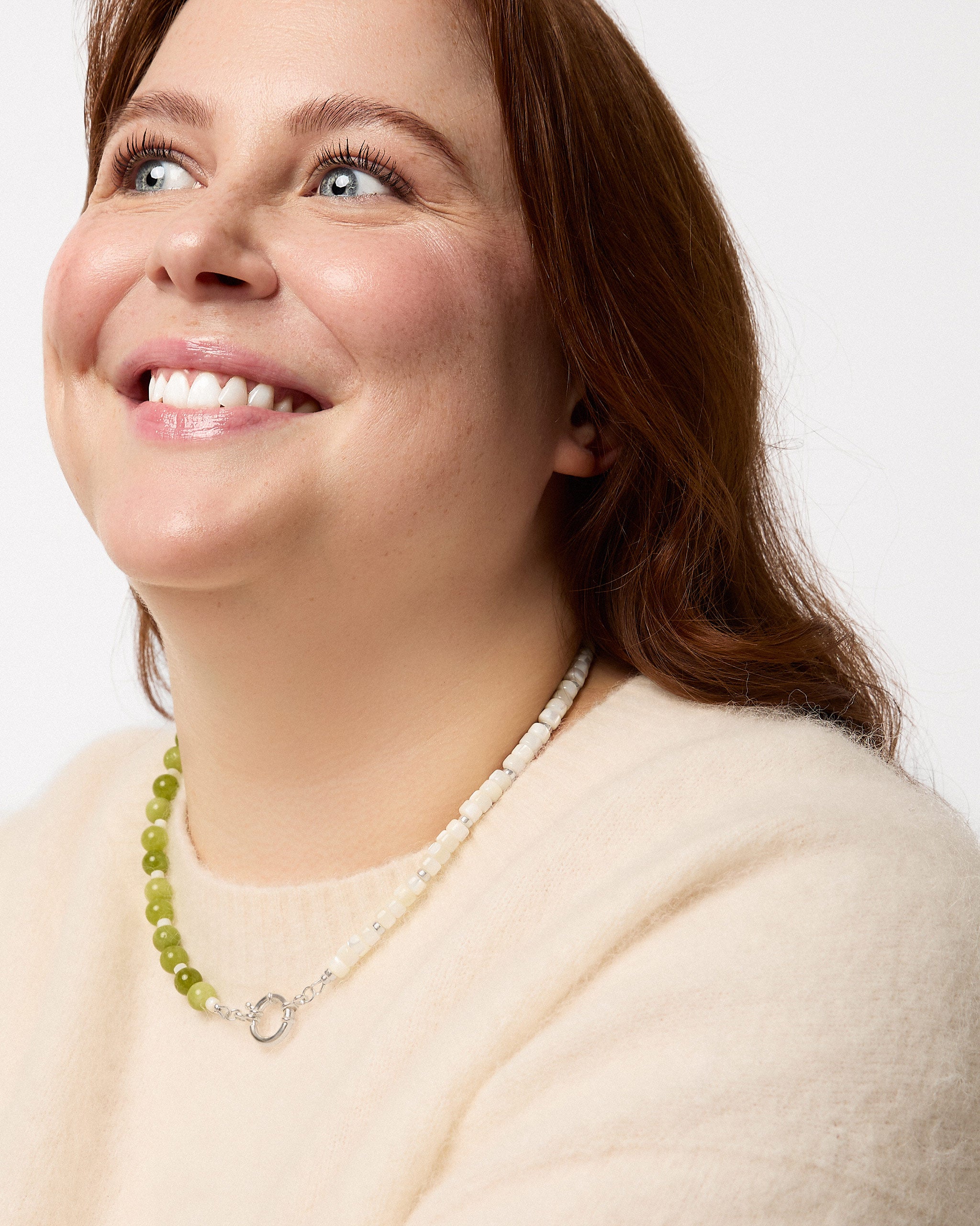 Woman wearing a beige sweater and green beaded necklace against a white background