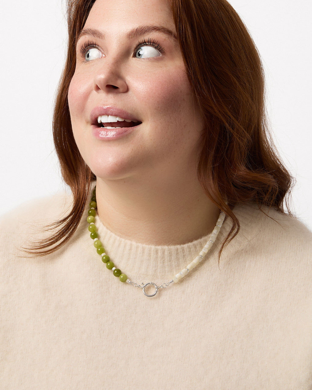 Woman wearing a necklace with green beads and a beige sweater on a white background
