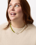 Woman wearing a necklace with green beads and a beige sweater on a white background