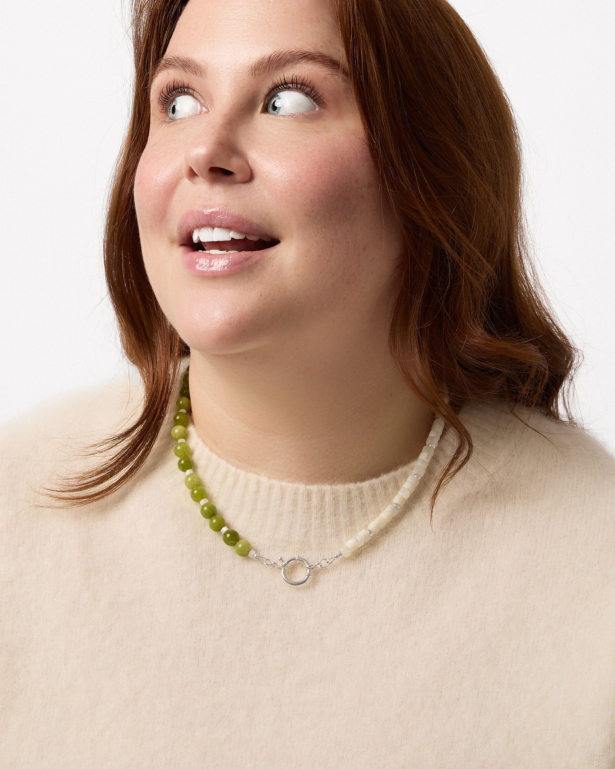 Woman wearing a necklace with green beads and a beige sweater on a white background