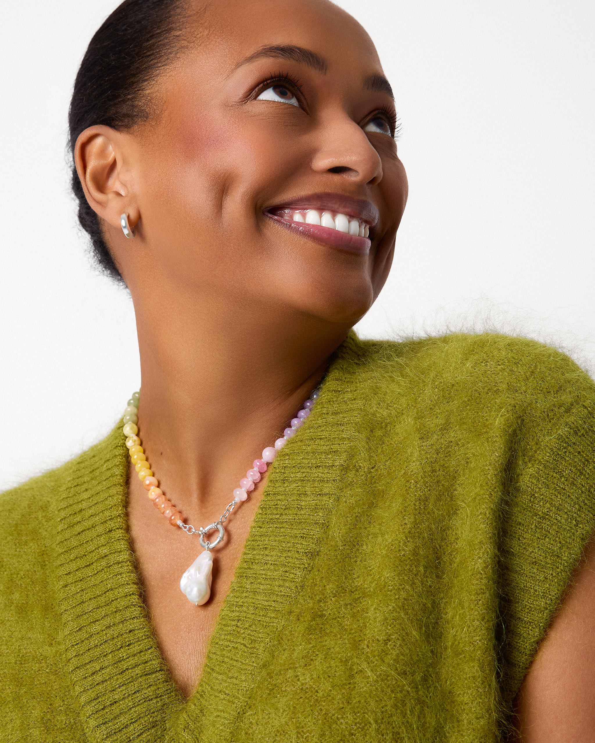 Woman wearing a green vest and colourful necklace against a white background