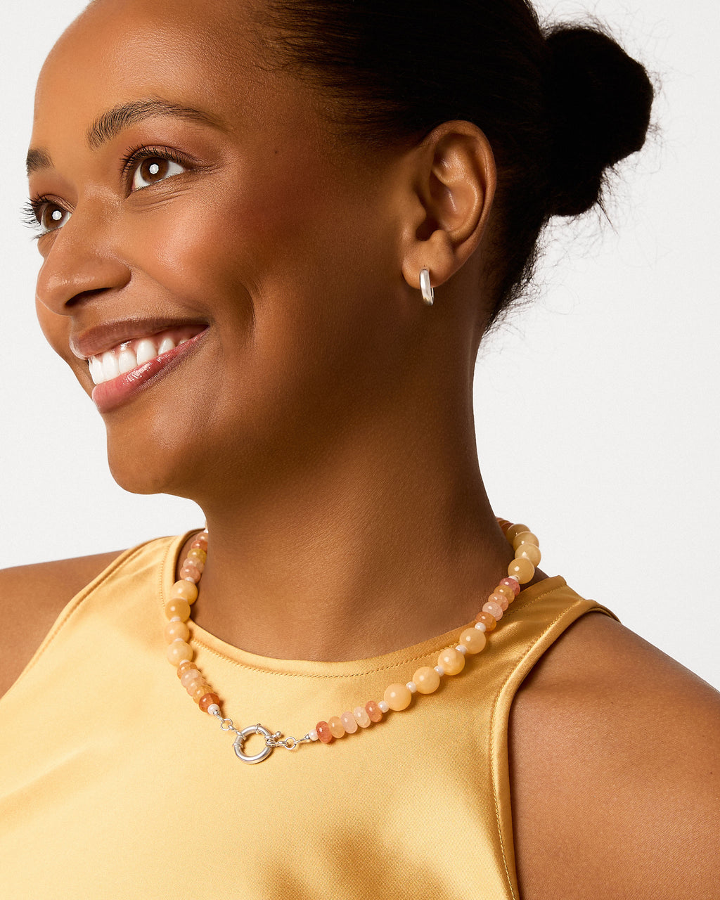 Woman wearing a yellow dress and beaded necklace against a plain background